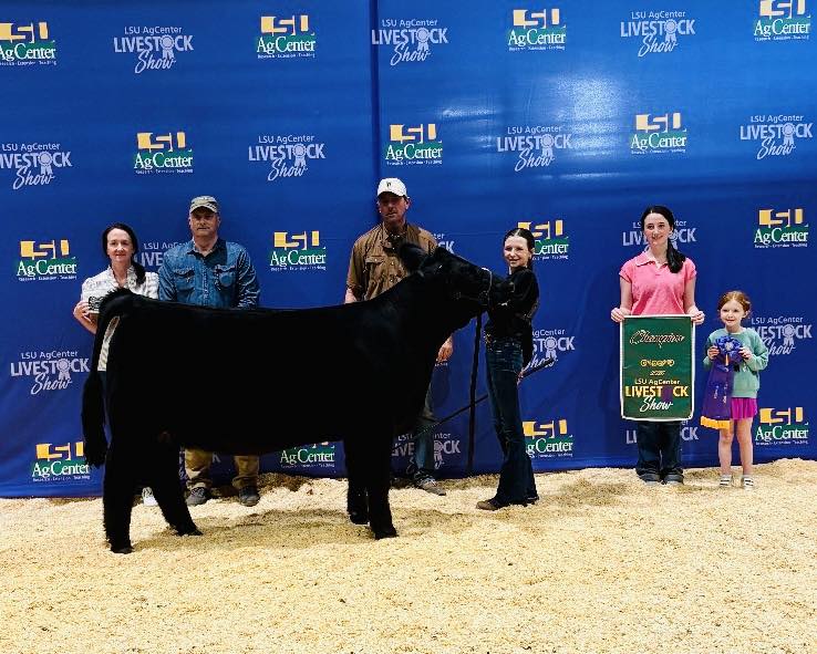 A group of people posing with a black cow.